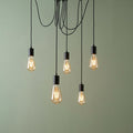 Five-light industrial spider pendant with black cables and exposed filament bulbs against a sage green wall.