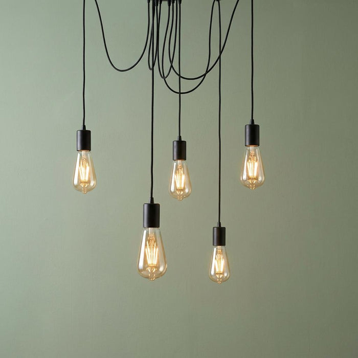 Five-light industrial spider pendant with black cables and exposed filament bulbs against a sage green wall.
