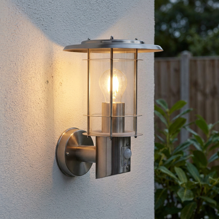 Stainless steel outdoor PIR wall light with a glowing bulb mounted on a white textured wall.
