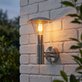 Modern stainless steel outdoor wall light with a PIR sensor illuminated against a white brick wall.