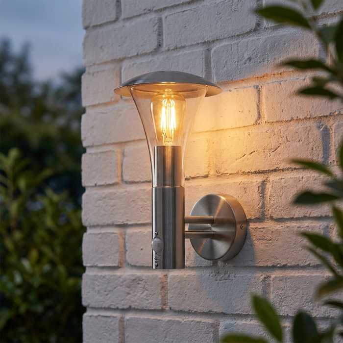 Modern stainless steel outdoor wall light with a PIR sensor illuminated against a white brick wall.