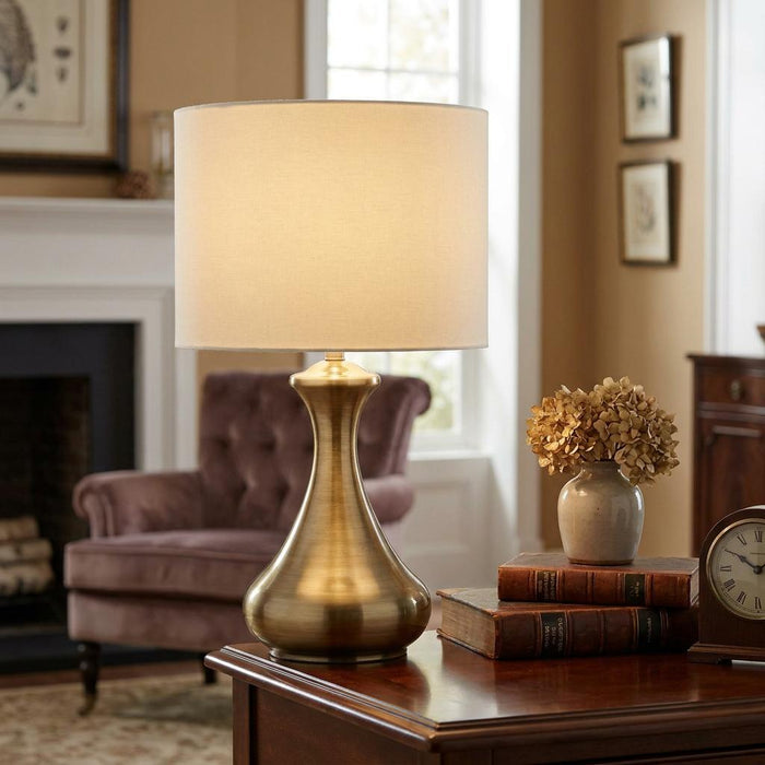 Antique brass touch lamp with a cream cylinder shade sits on a wooden side table in a cozy living room.