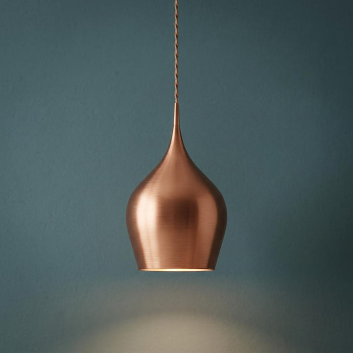 Brushed copper teardrop pendant light hanging against a teal wall, casting a warm glow downwards.