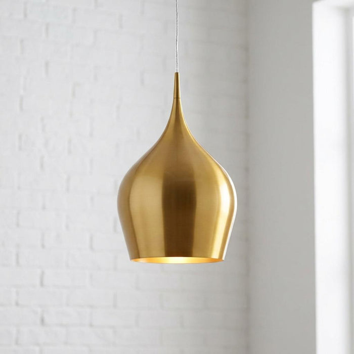 Brushed gold teardrop pendant light hanging in front of a white brick wall.