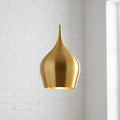 Brushed gold teardrop pendant light hanging in front of a white brick wall.