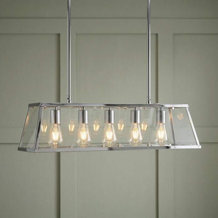 Five-light chrome lantern bar pendant with clear glass panels and exposed bulbs against a green paneled wall.