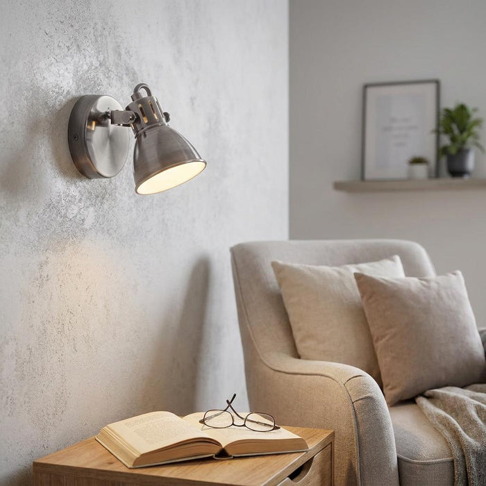 Antique nickel wall spotlight illuminating an open book in a modern reading nook with a textured gray wall.