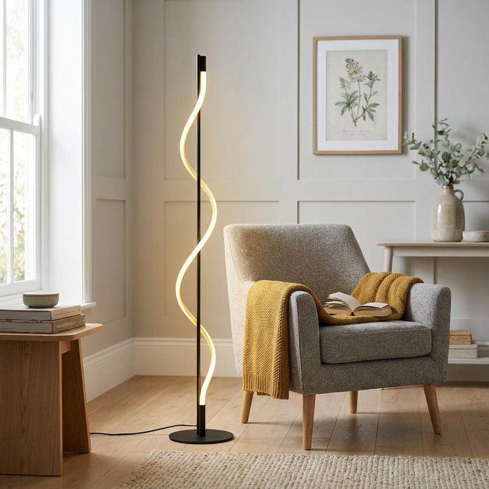 Serpent black modern LED floor lamp with a glowing wave-like light stand in a cozy living room next to a gray armchair.