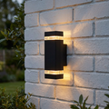 A black up and down wall light with crystal glass inserts illuminates a white brick wall outdoors.