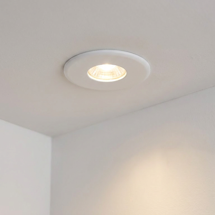 Lit ShieldPLUS white recessed ceiling downlight casting a warm glow on a white ceiling.