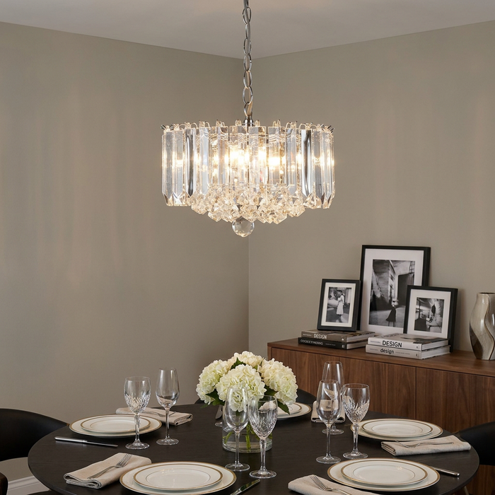 Modern chrome and acrylic 4-light chandelier hanging over an elegantly set dining table with white flowers.