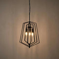 Black metal geometric pendant light with three candle bulbs against a warm, neutral wall.