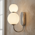 Snowball 2 wall light in chrome with two glowing opal glass globes on a textured wall.