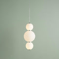 A vertical pendant light with three stacked opal glass globes on a chrome frame against a light green wall.