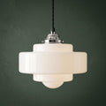Tiered opal glass Art Deco pendant light with a chrome gallery hanging against a dark green background.
