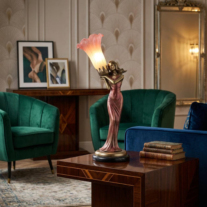 Sofia Brass Art Deco Figurine Lamp with a pink lily shade, displayed on a wooden table in a stylish living room.