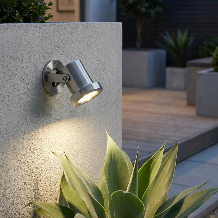 Stainless steel outdoor spotlight mounted on a concrete wall, illuminating a succulent plant in a modern garden.