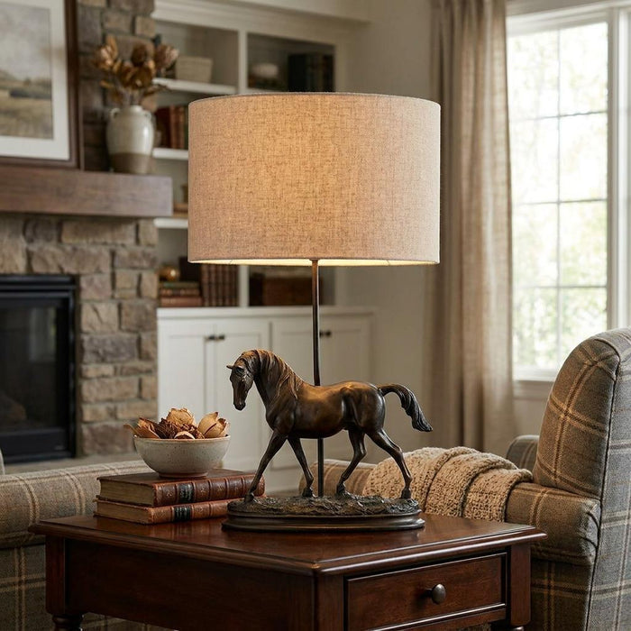 Bronze horse sculpture table lamp with a natural linen shade on a wooden side table in a cozy living room.