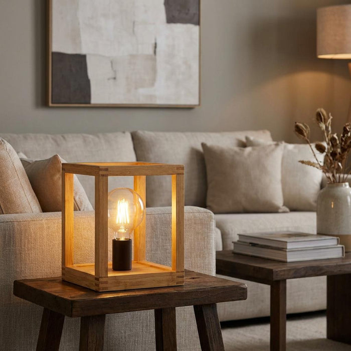 Square bamboo table lamp with a glowing bulb on a rustic wooden side table in a modern living room setting.