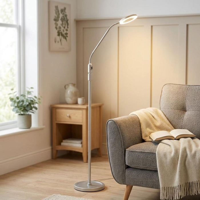 Silver LED floor reading lamp illuminating a cozy gray armchair with an open book in a bright living room.