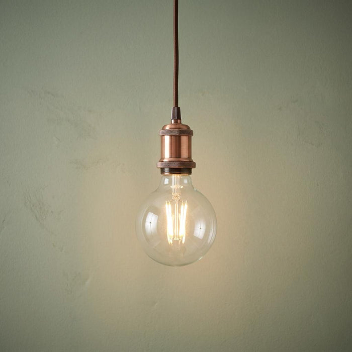 Illuminated clear globe bulb with copper socket and fabric cable against a textured green background.