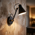 Matte black and gold adjustable swing arm wall light illuminated against a distressed textured wall.