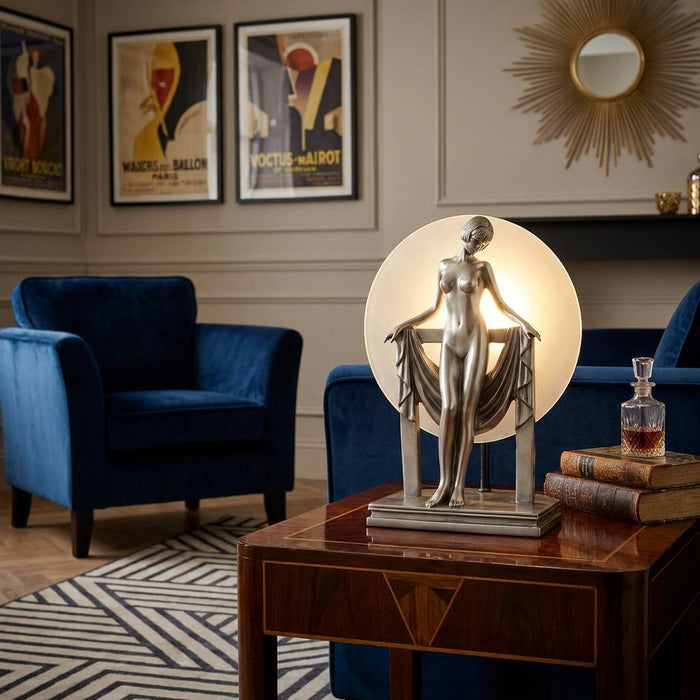 Art Deco silver figurine lamp with a circular frosted glass light on a wooden table in a living room setting.