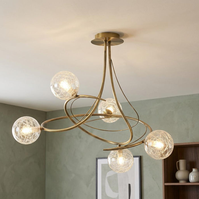 Tabia 5 light antique brass semi flush ceiling light with swooping arms and webbed glass globes in a modern room.