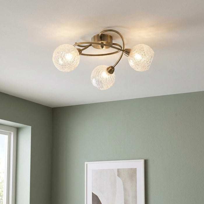 Tarn 3 light antique brass flush ceiling light with crackle glass globes on a light green wall.