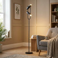 Modern black floor lamp with two adjustable spotlights illuminating a neutral living room with an armchair.