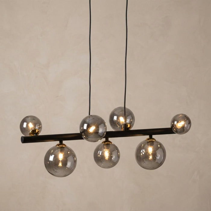 Tere 7-light pendant with smoked glass globes on a black horizontal bar with gold accents against a neutral wall.