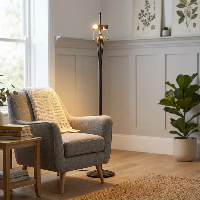 Bronze floor lamp base with lit bulbs beside a grey armchair in a neutrally decorated, cozy reading corner.