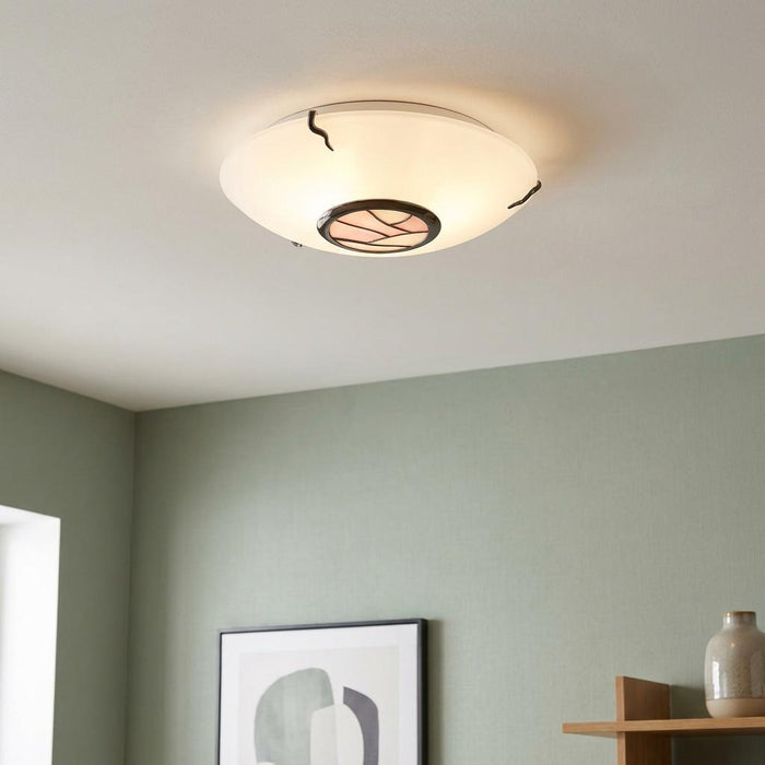 Illuminated Tiffany flush mount ceiling light with a white glass dome and pink mosaic detail on a green wall.