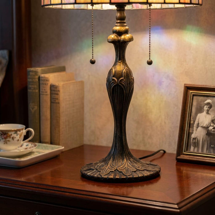 Ornate bronze Tiffany lamp base on a wooden desk alongside vintage books and a framed photograph.