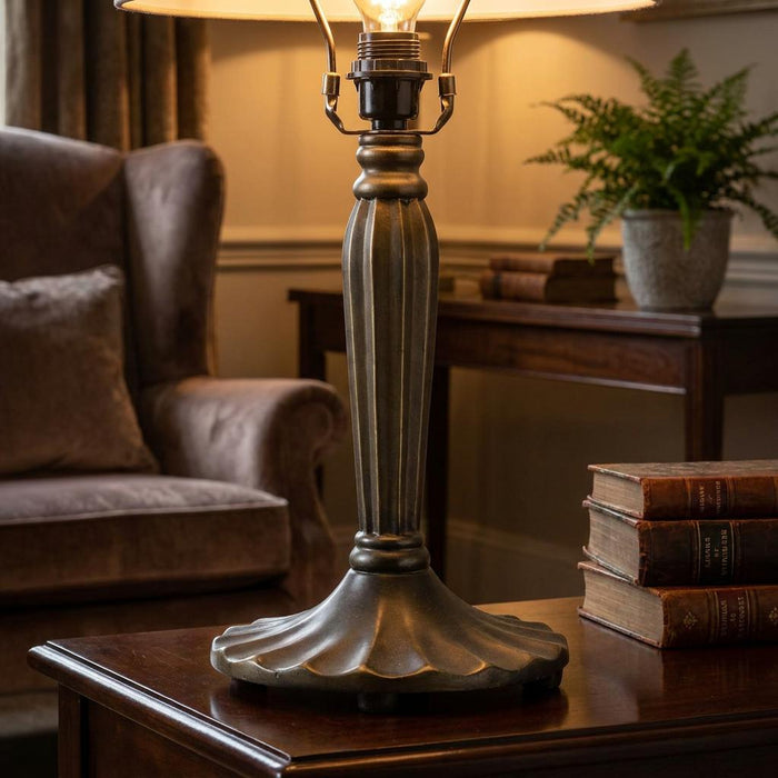 Antique bronze fluted table lamp base on a dark wood desk with vintage books in a warmly lit room.