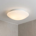 Modern white opal glass flush ceiling light illuminated in a minimalist bathroom corner.