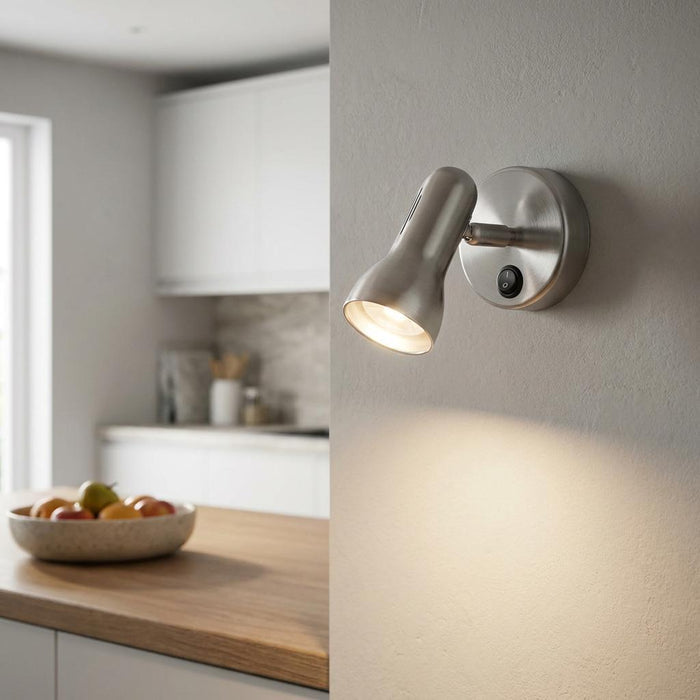 Satin chrome adjustable wall spotlight with a toggle switch, illuminated in a modern kitchen setting.
