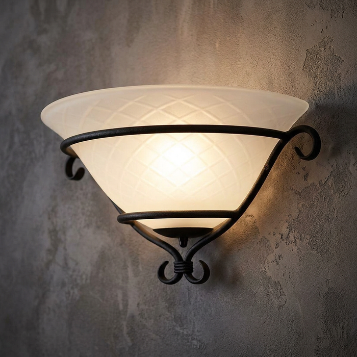 Black scrollwork wall uplighter with a frosted cross-hatch glass bowl glowing on a textured wall.