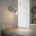 Illuminated chrome and glass wall spotlight casting light onto a stone countertop in a modern interior.