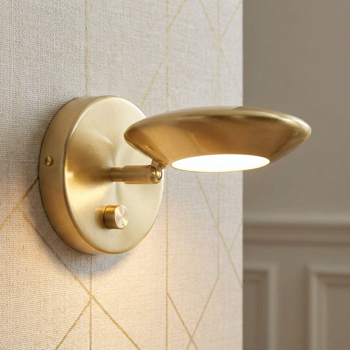 Satin brass adjustable wall light with integrated dimmer switch mounted on a geometric patterned wall.