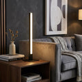 A sleek black Tribeca LED table lamp glowing on a wooden side table next to a grey sofa in a modern living room.