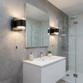 Two black up/down wall lights with cord pulls flanking a bathroom mirror above a white vanity in a grey tiled room.