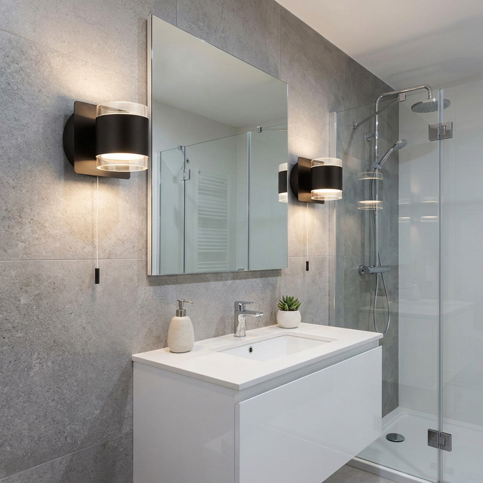 Two black up/down wall lights with cord pulls flanking a bathroom mirror above a white vanity in a grey tiled room.