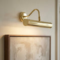 A polished brass LED picture light mounted on a wall, illuminating a framed piece of art.
