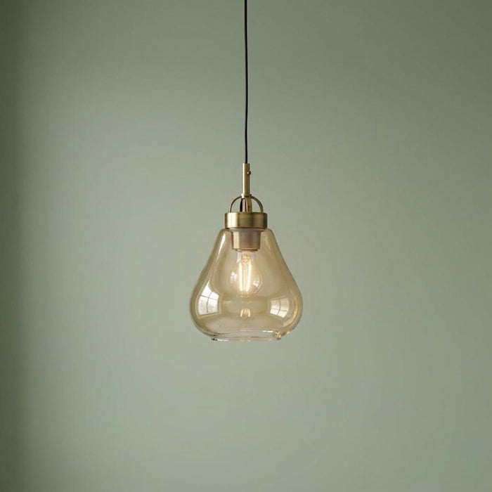 Turua antique brass pendant light with a teardrop amber glass shade hanging against a sage green wall.