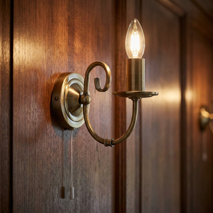 Tuscany antique brass wall light with a glowing candle bulb mounted on a dark wood-paneled wall.