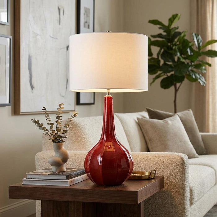 Upton Large Red Ceramic Table Lamp with a white drum shade on a wooden side table in a modern living room.