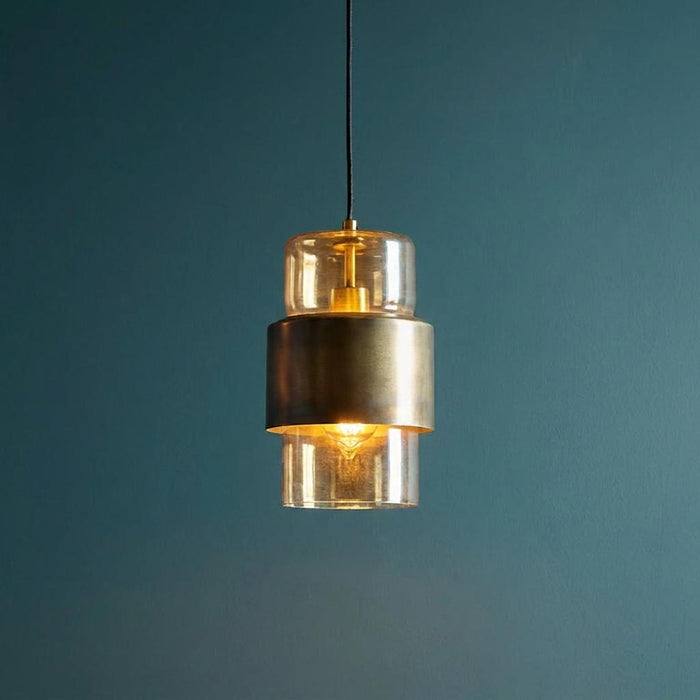 Modern brass patina pendant light with champagne glass cylinders hanging against a dark teal wall.