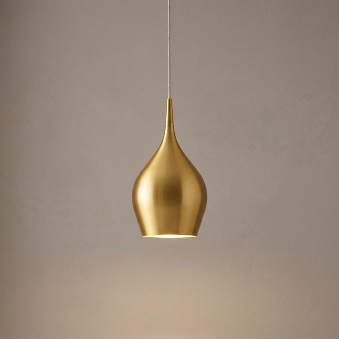 A modern teardrop-shaped gold metal pendant light illuminated against a neutral wall.