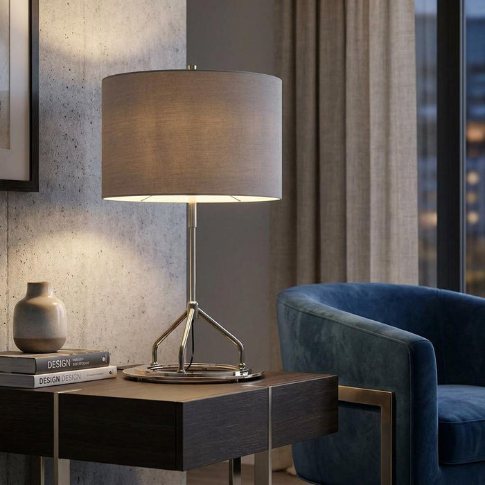 Polished nickel table lamp with a neutral drum shade glowing on a side table in a modern living room.